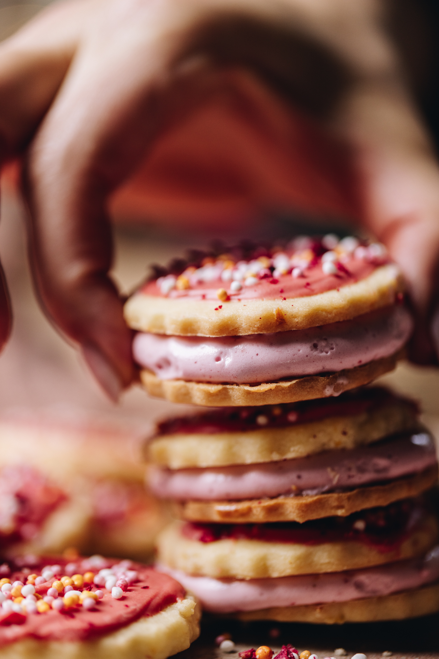 A hand is stacking hundreds and thousands biscuits that are filled with marshmallow. There is three in a pile.