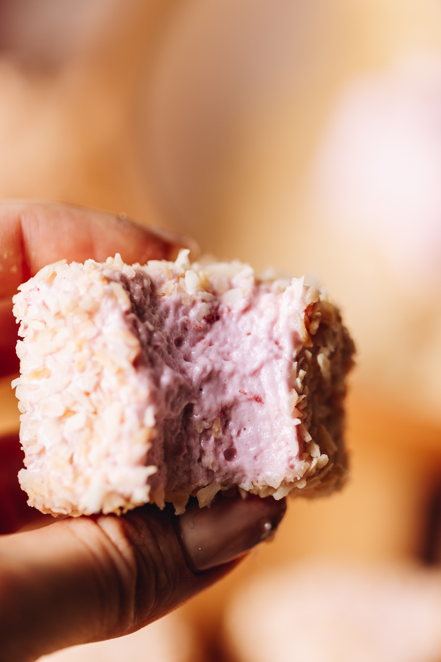 A close up shot reveals a square of egg-free Raspberry marshmallow that has been bitten in to and is covered in toasted coconut. 