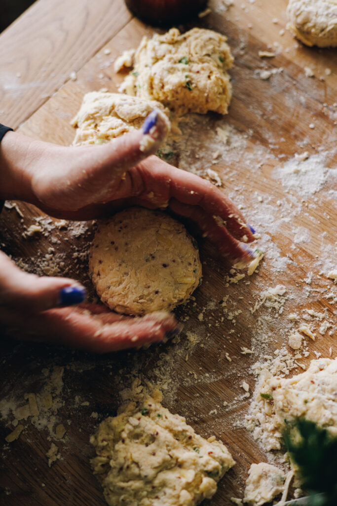 A top shot of a piece of the Brie Stuffed Honey Mustard Scone dough being shaped in to a round. It is sitting on a heavily floured, wooden bench. 
