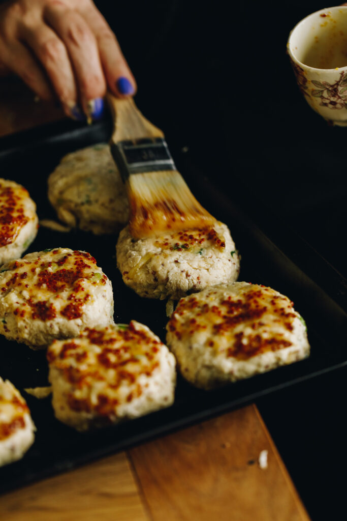 The Brie Stuffed Honey Mustard Scones are arranged on a black tray. Most of them have honey mustard glaze on top, one of the scones is being glazed with a pastry brush.