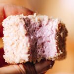 An extreme close up of a piece of egg-free marshmallow has had a piece bitten out of eat showing the short inside texture, it is covered int toasted coconut.