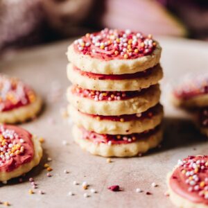 Freshly baked and decorated hundreds and thousands biscuits are piled on top of each other.