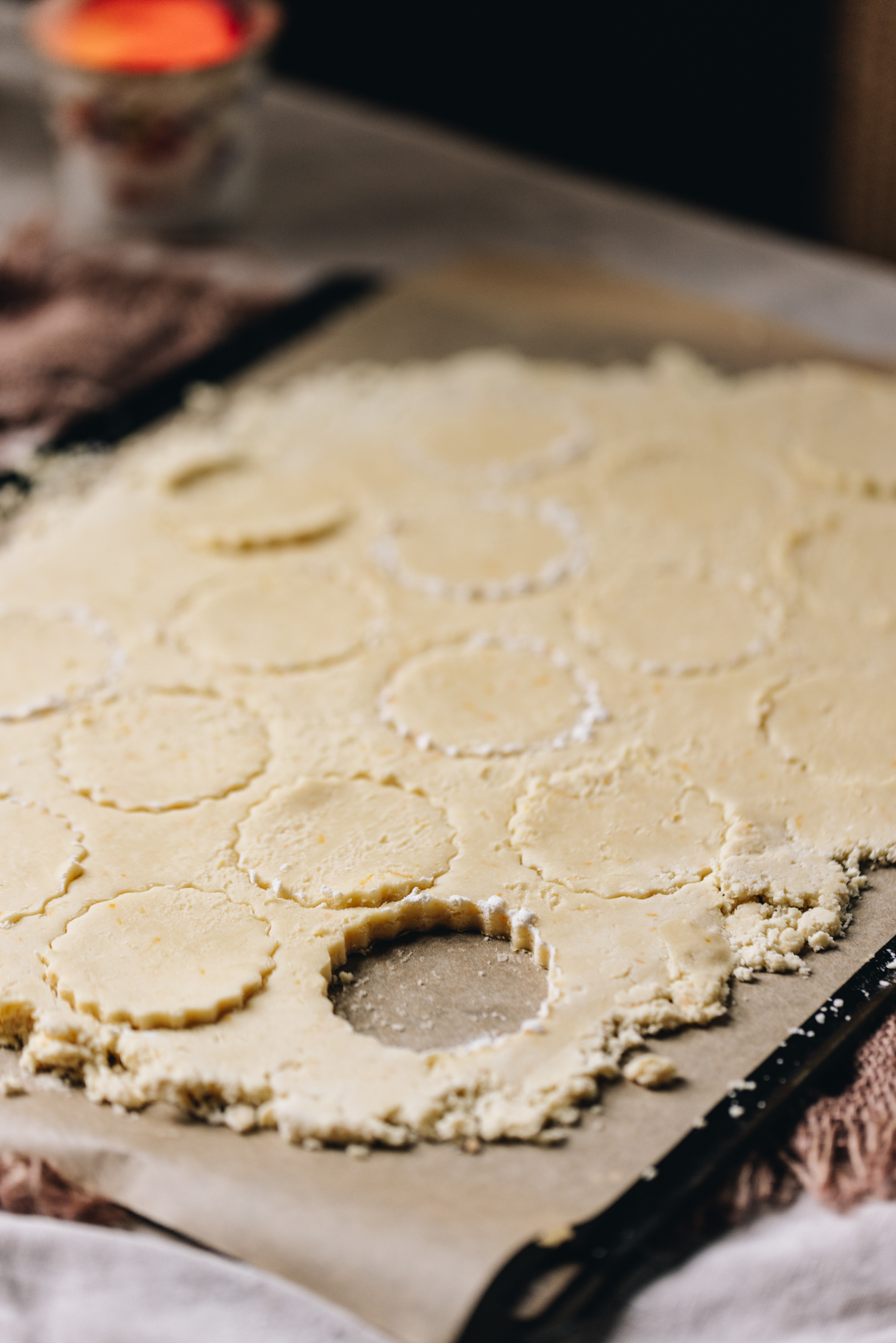 On a black tray with brown baking paper is hundreds and thousands biscuit dough cut out with a crinkled cookie cutter.