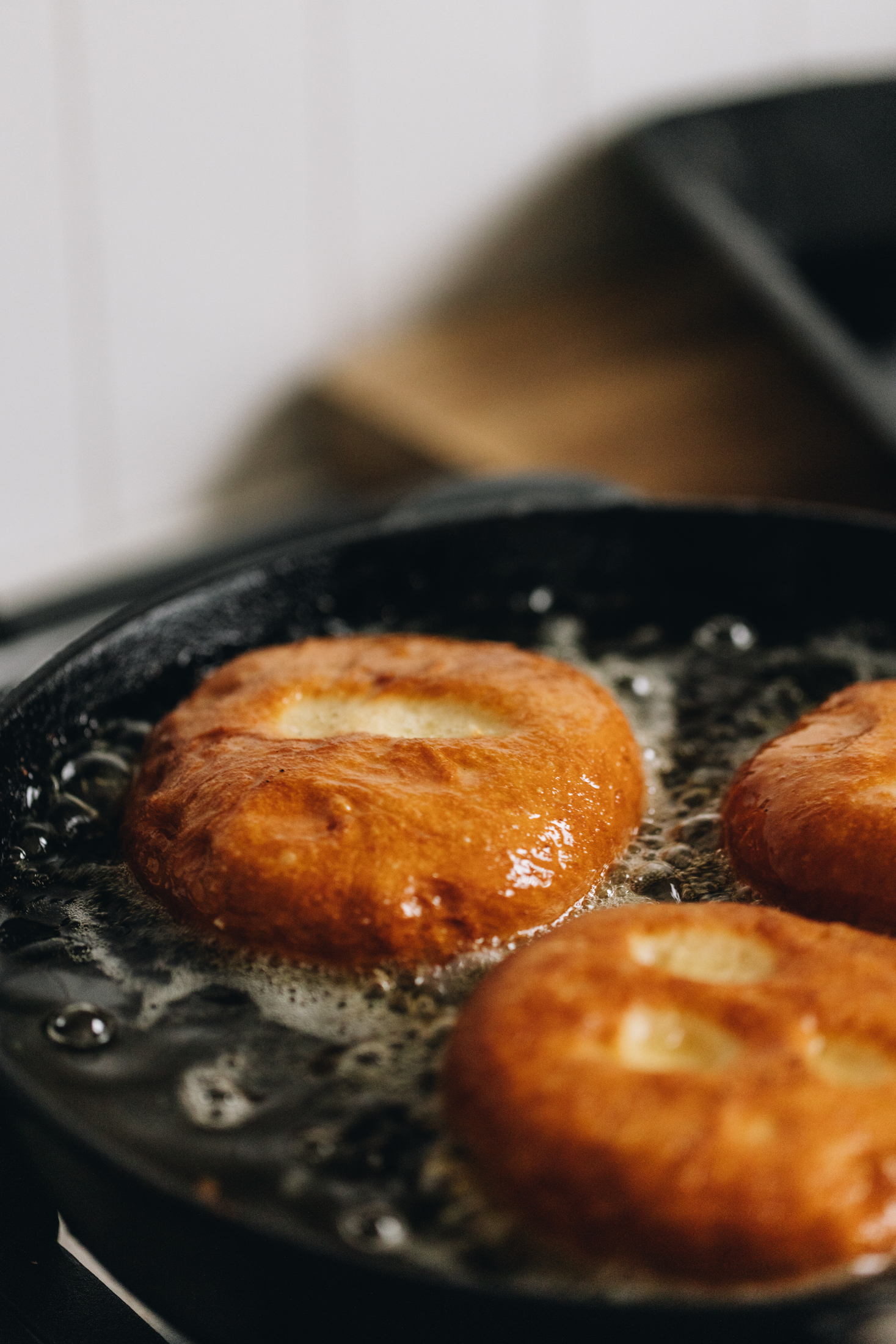 In a black cast iron pan is three pieces of golden chocolate stuffed fry bread frying in bubbly oil. 