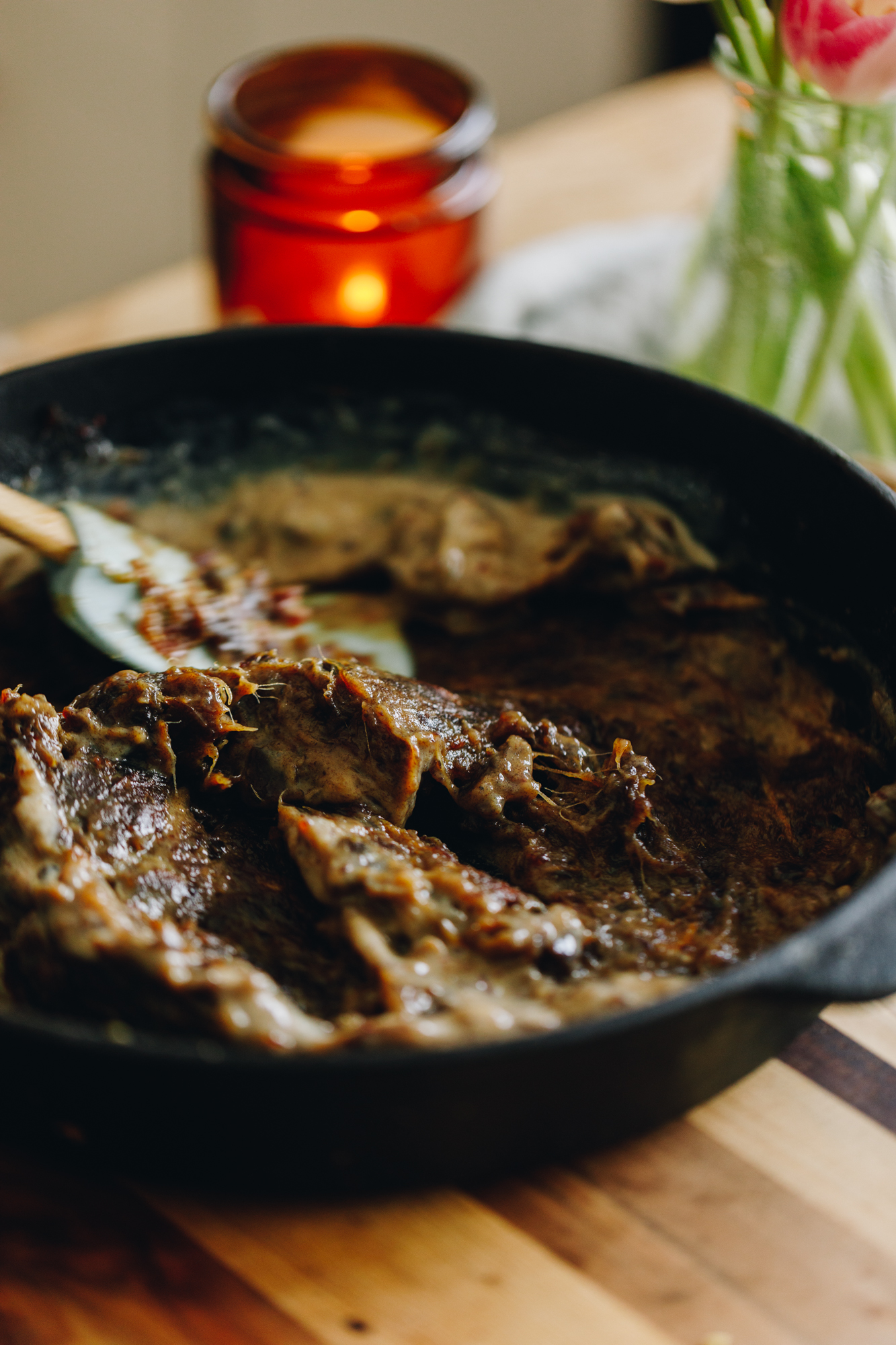 A cast iron pan sits on a wooden striped board with a candle in the background. In the pan is mashed dates with milk mixed through it. 