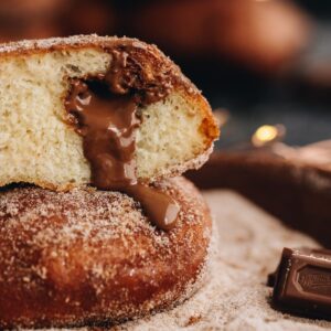 Close up of chocolate stuffed fry bread, it is cut open and is sitting on a bowl of cinnamon sugar. Gooey chocolate is oozing out of the centre of one of the pieces.