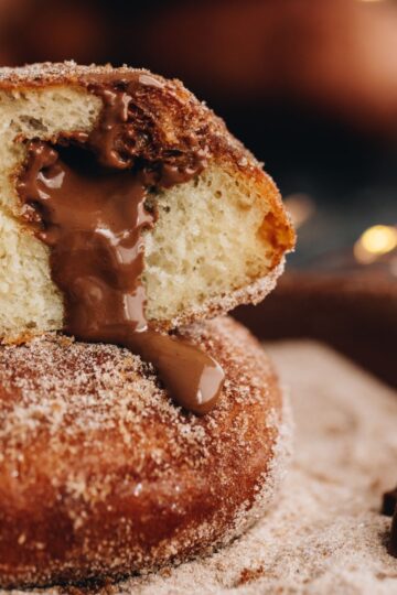 Close up of chocolate stuffed fry bread, it is cut open and is sitting on a bowl of cinnamon sugar. Gooey chocolate is oozing out of the centre of one of the pieces.