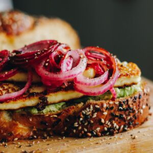 Close up shot of freshly baked bread with bagel season on top shows layers on avocado, grilled halloumi cheese and red pickled onions.