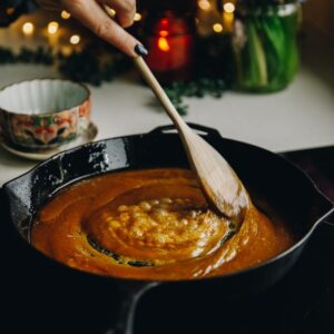 In a black cast iron pan is easy caramel sauce simmering, it is being stirred with a wooden spoon.