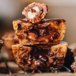 Close up gooey cookies pies that have been sliced open and stacked on top of each other. The gooey chocolate centre is oozing out. Half of a ferro rocher is on top.