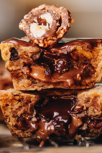 Close up gooey cookies pies that have been sliced open and stacked on top of each other. The gooey chocolate centre is oozing out. Half of a ferro rocher is on top.