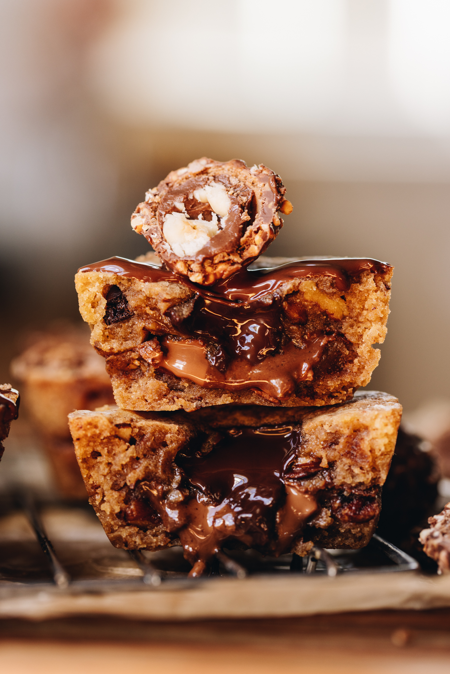 Close up gooey cookies pies that have been sliced open and stacked on top of each other. The gooey chocolate centre is oozing out. Half of a ferro rocher is on top.