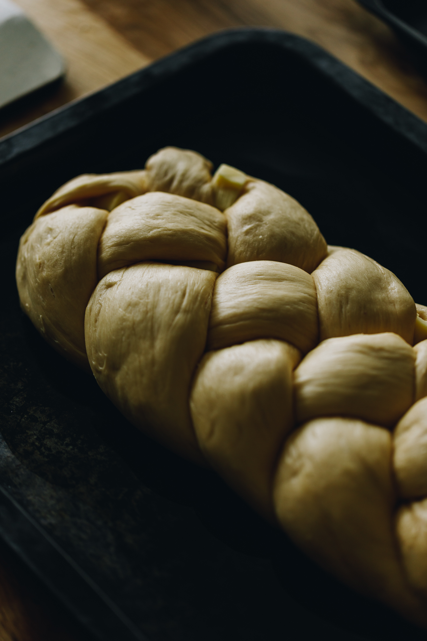 On a black tray is a savoury braided brioche loaf that is braided tightly. A little bit of cheese can be seen poking out in places. 