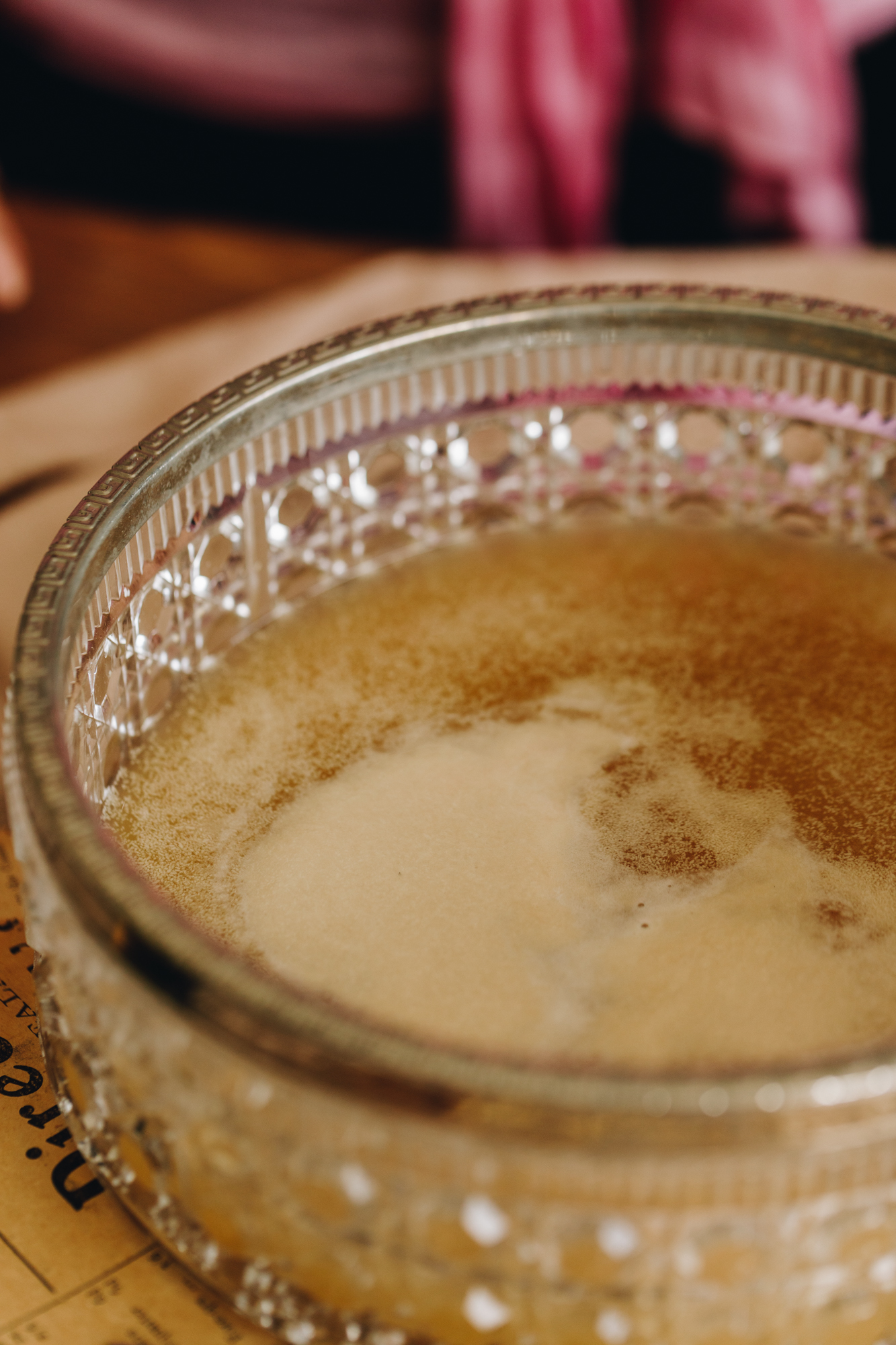 A glass vintage bowl with a silver trim sits on a wooden table. In the bowl is activated yeast.