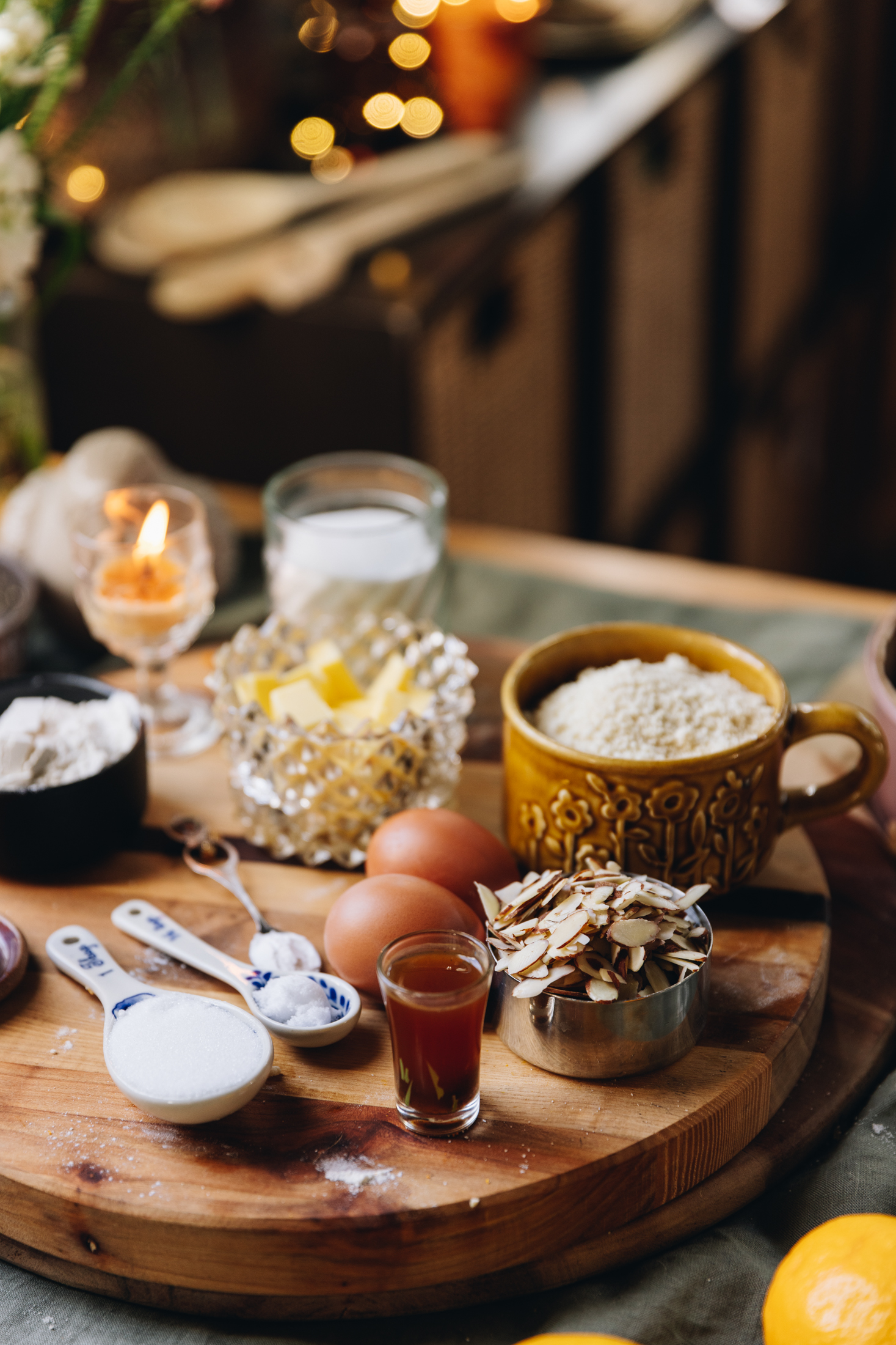 On a wooden board sits vintage bowls and small plates that have cake ingredients on it. There is eggs, sliced almonds, ground almonds and sugar in view.