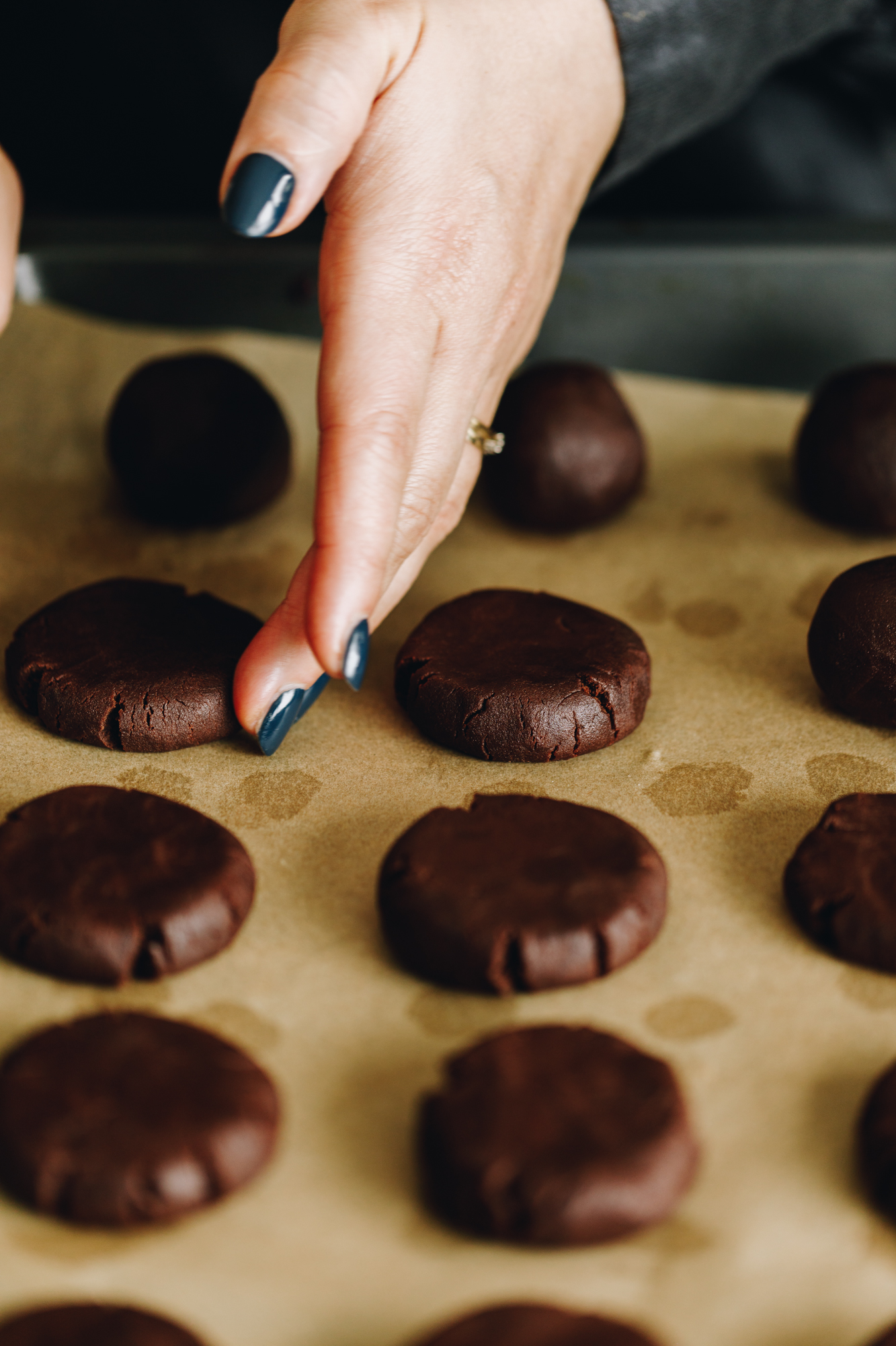 On a tray with brown baking paper are unbaked chocolate cookies that have been flattened down. 