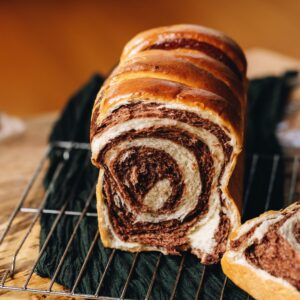 A baked chocolate swirl bread loaf cut open is on a cooling track revealing the chocolate swirl.