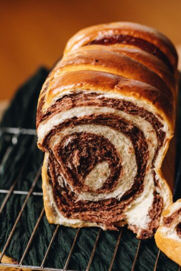 A baked chocolate swirl bread loaf cut open is on a cooling track revealing the chocolate swirl.