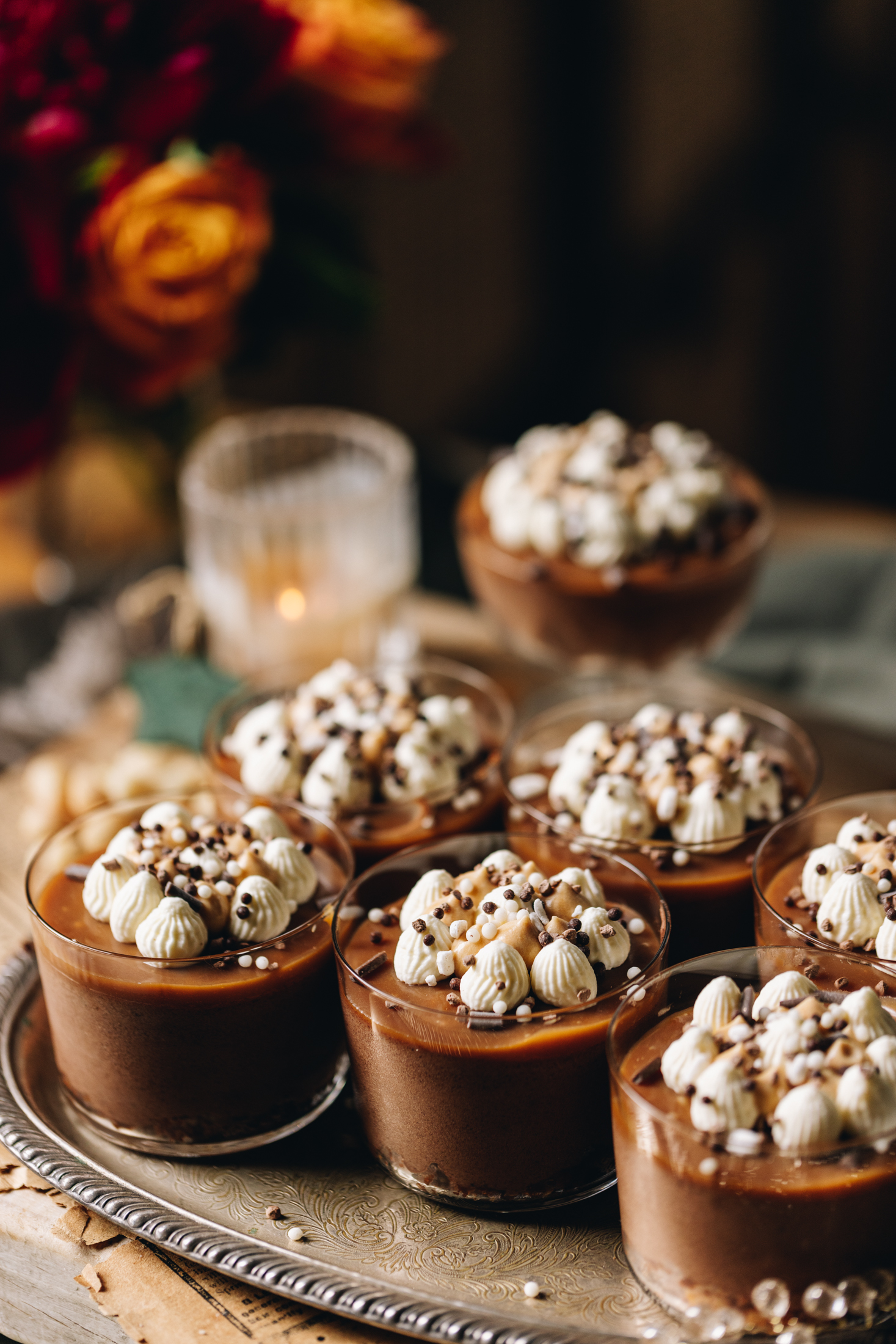 The Chocolate Mousse and Caramel Desserts are served on a silver tray with flowers in the background and a candle.