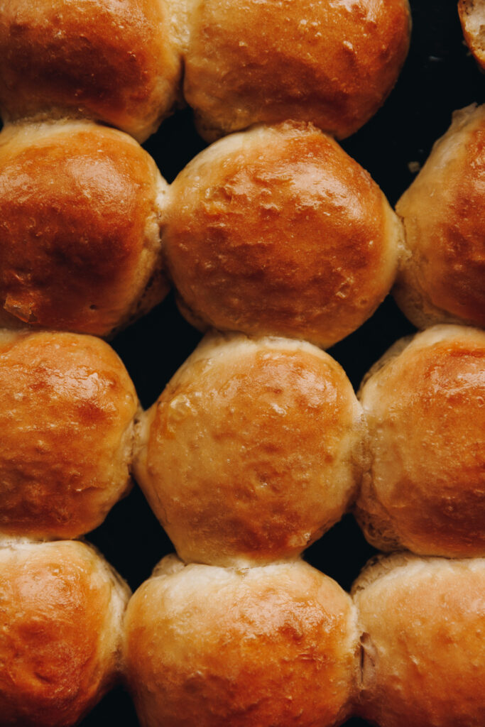 A flat lay shot shows freshly baked no-knead bread buns on a tray. They are golden and have a shiny, buttery top. 
