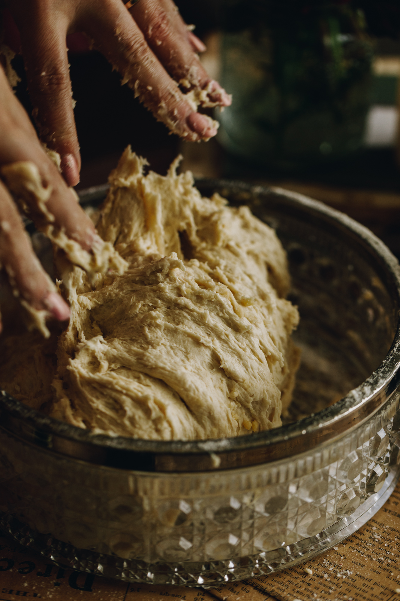 Sticky fingers are in a bowl kneading bread dough. It is in a vintage glass bowl. 