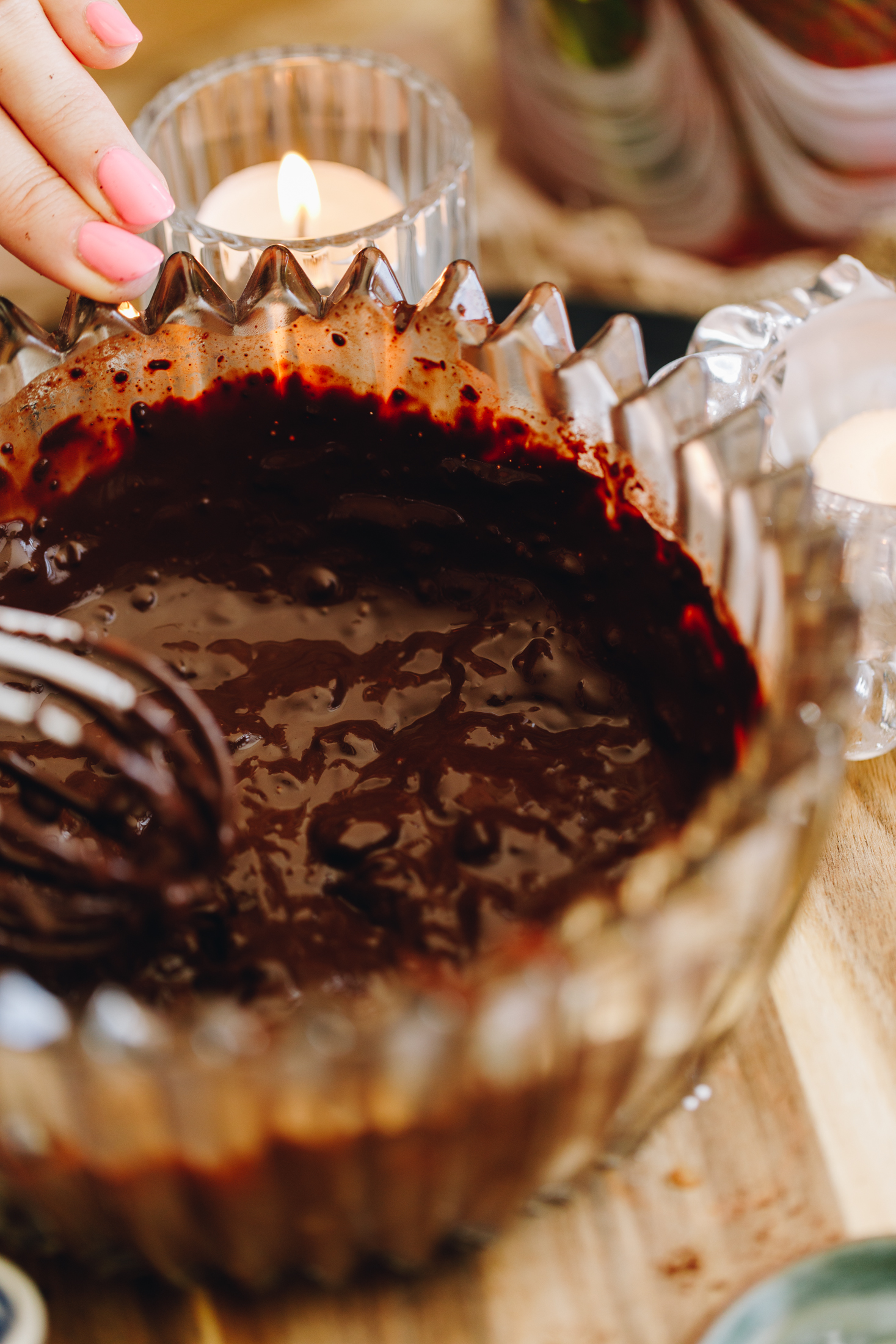 A vintage glass bowl has a thick cocoa mixture in it. It sits on a striped wooden bowl. 