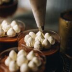 Stable whipped cream is being piped in to peaks on top of a caramel dessert.