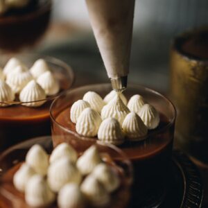 Stable whipped cream is being piped in to peaks on top of a caramel dessert.