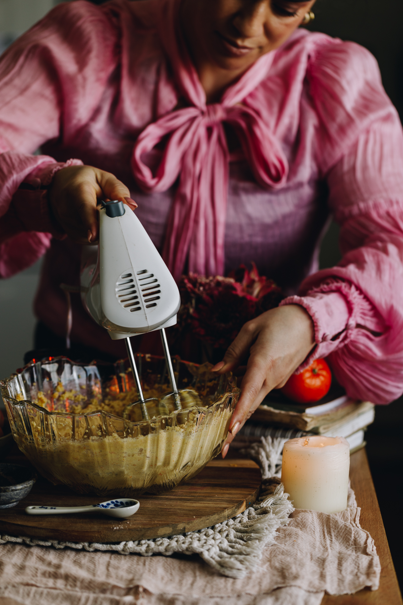 The butter and sugar for the Raspberry Lamington Cake is being whipped together in a glass bowl that is sitting on a wooden board. Naomi Toilalo can be seen doing the action.