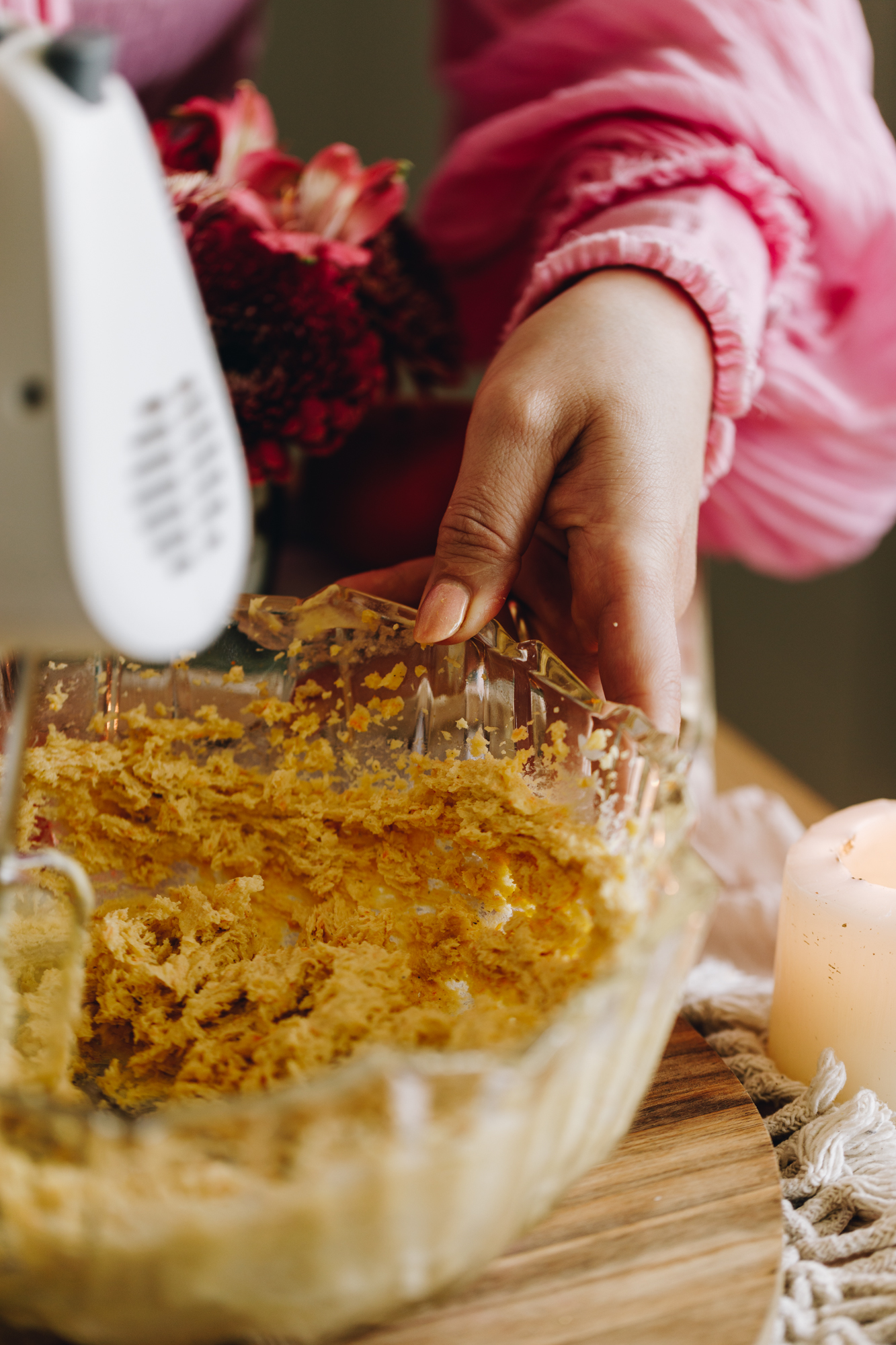A close of the butter and sugar being whipped together in a glass bowl that is sitting on a wooden board.
