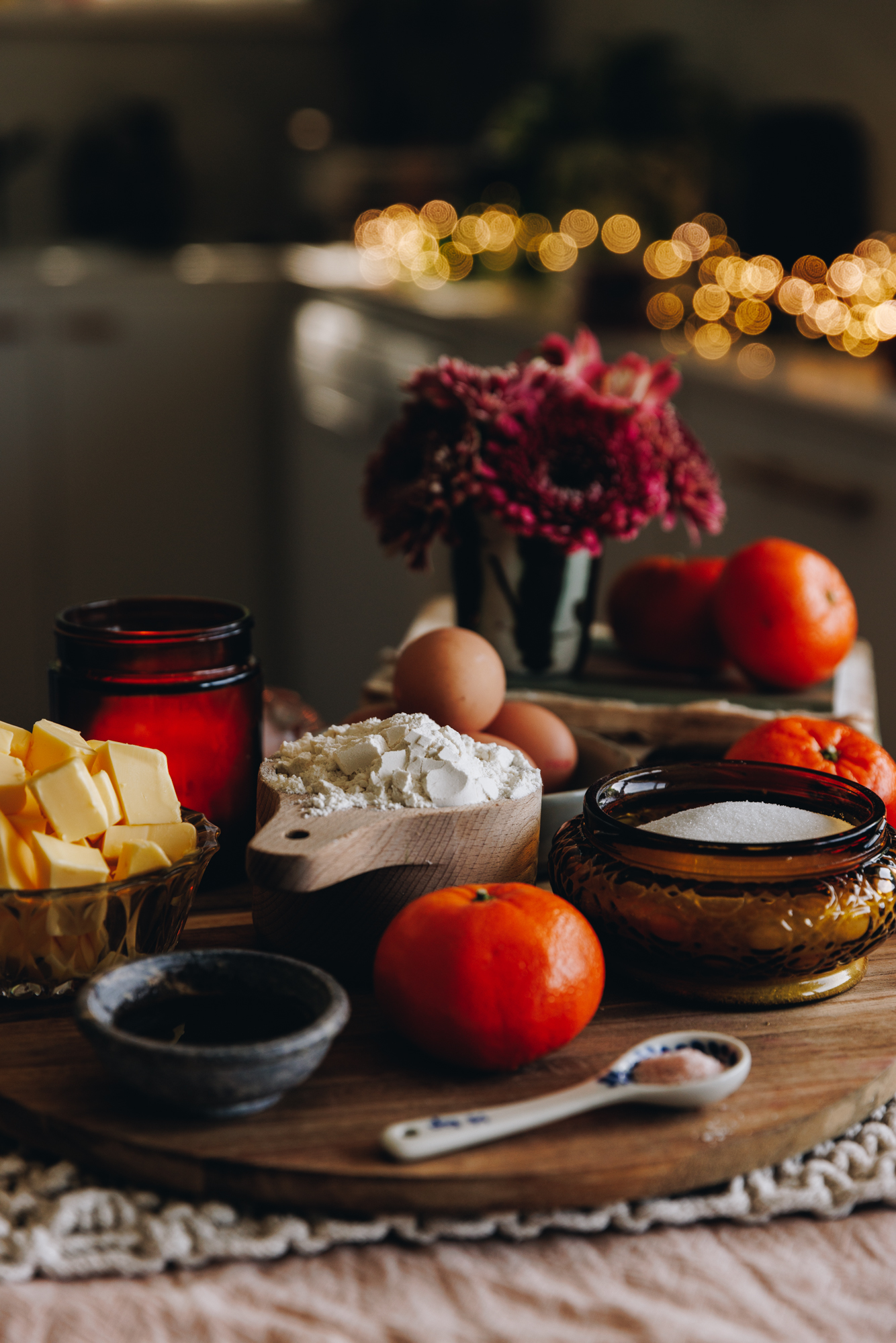 The ingredients for the Raspberry Lamington Cake are in different vintage bowls and are sitting on a wooden board. A amber candle and pink flowers are behind the ingredients.