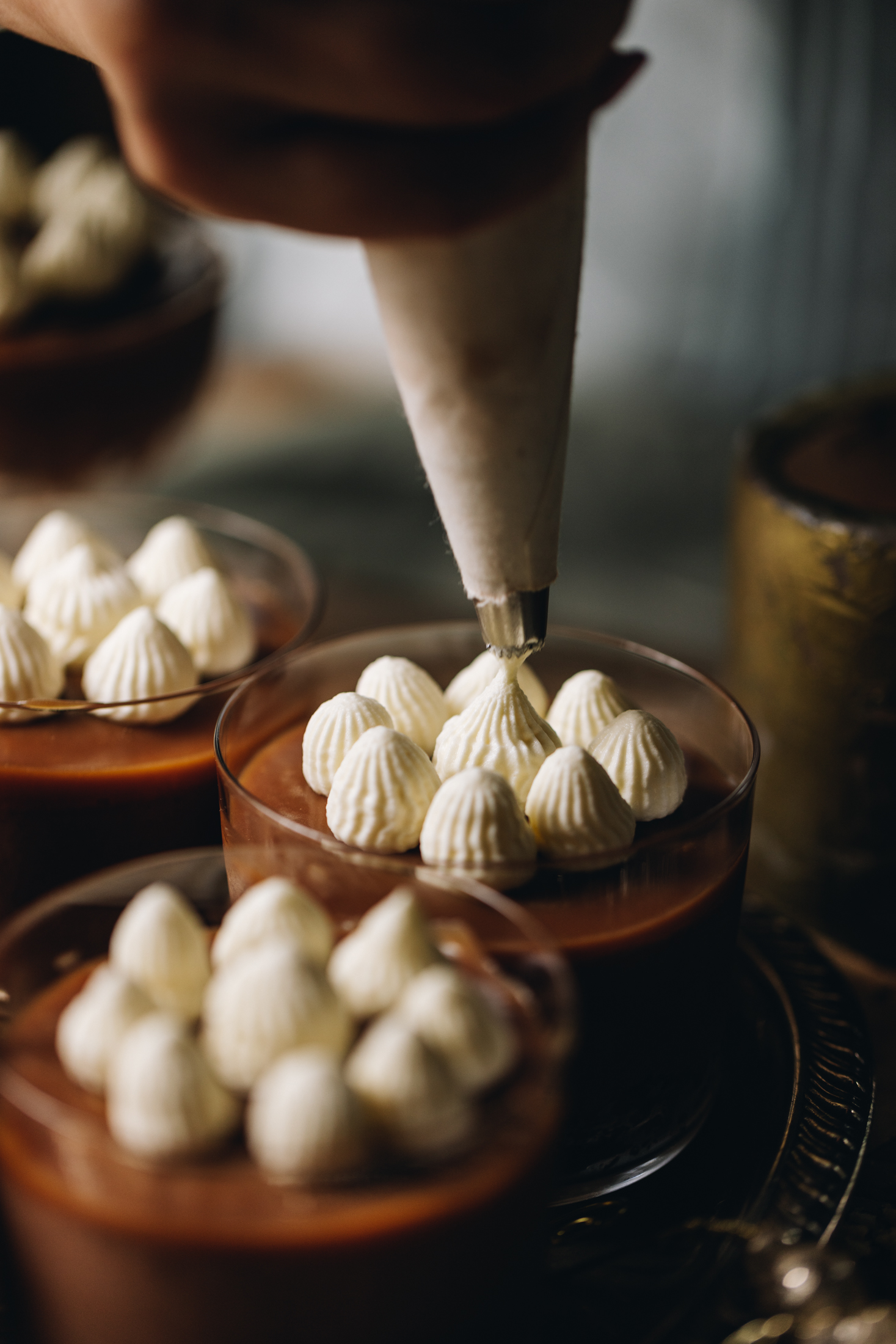 Stable whipped cream is being typed on to chocolate mousse. The piped peaks can be seen clearly on the desserts. 