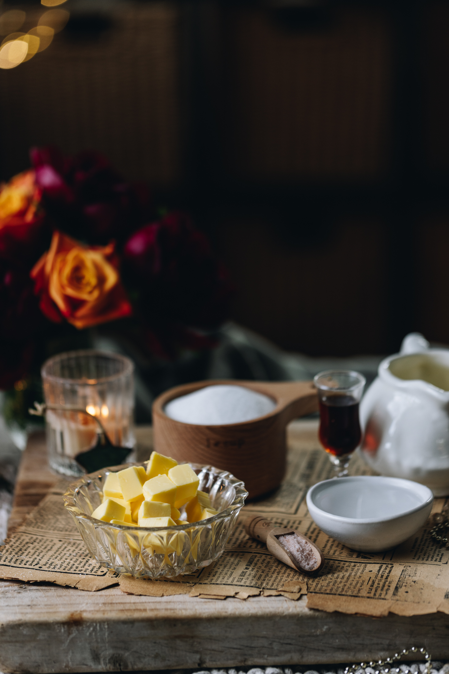 Homemade Salted Caramel Sauce ingredients are in different vintage bowls and are sitting on a wooden board with old newspaper under it. 
