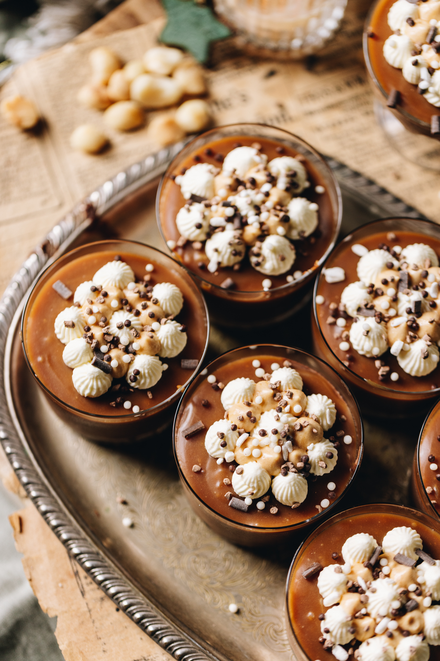 A top shot shows the homemade salted caramel sauce on top of decorated desserts in glass jars that sit on a vintage tray on a wooden table. 