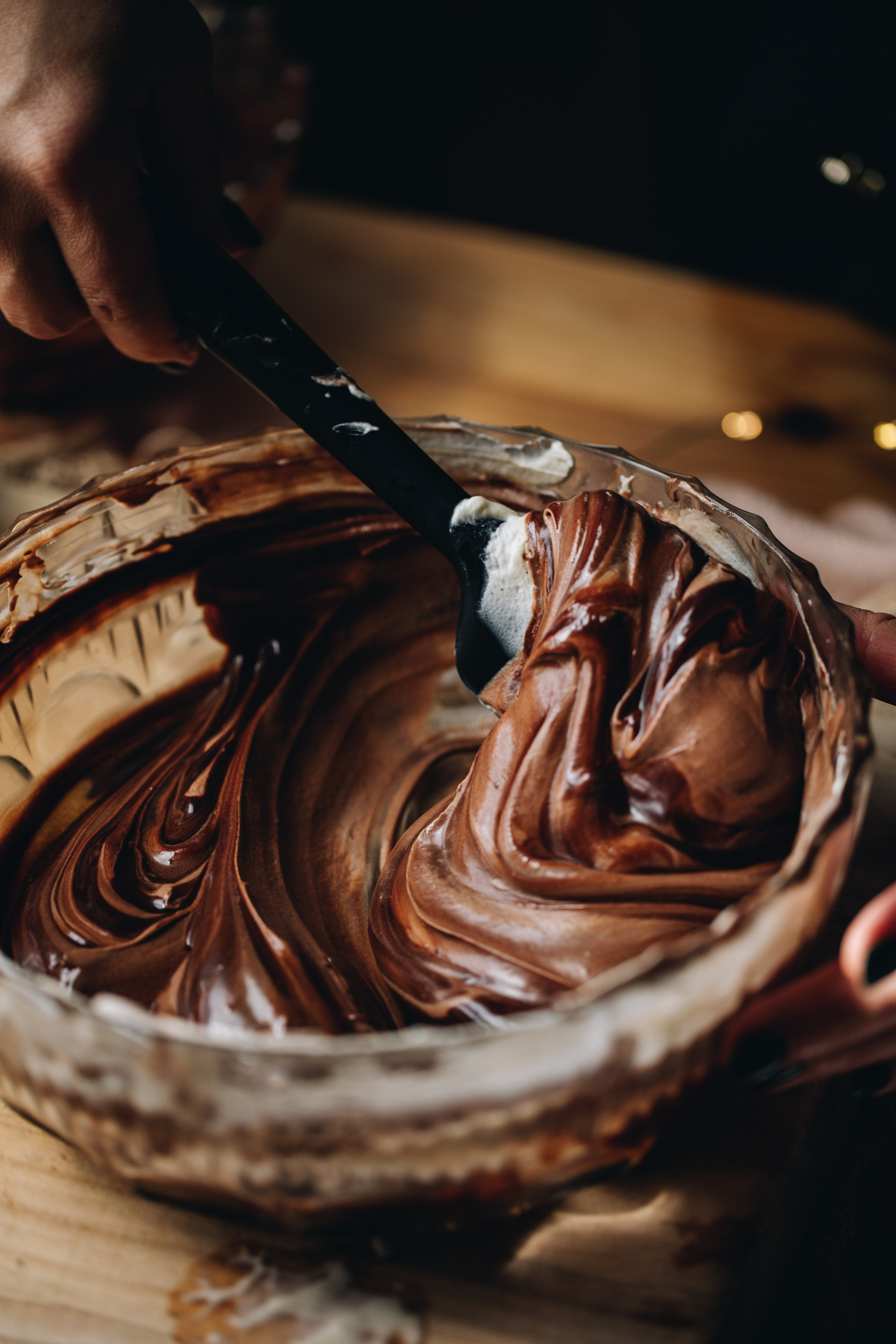 In a glass vintage bowl dark chocolate is being folded with cream, the mixture shows the streaks of ingredients being folded together. 