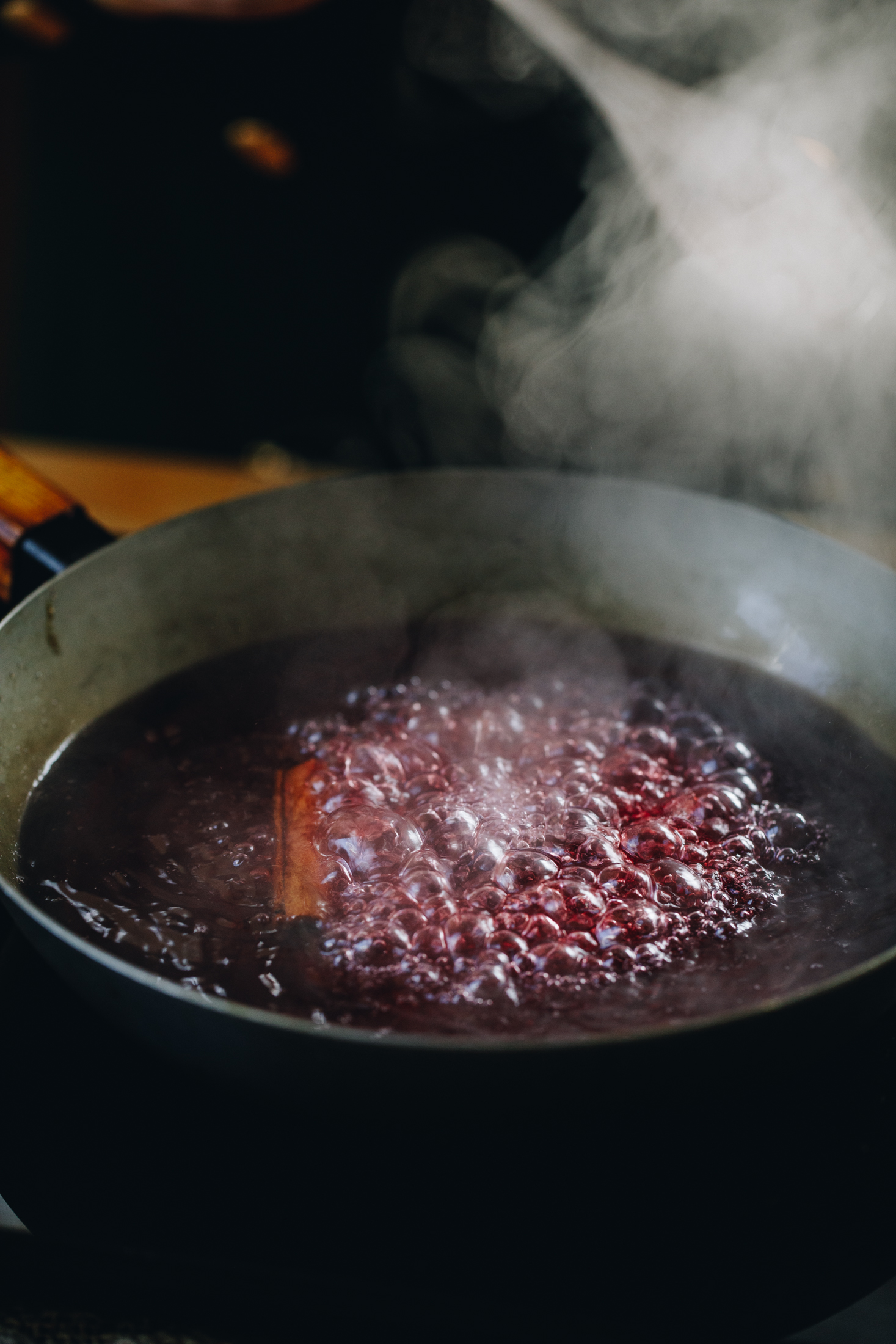 In a frying pan cranberry juice is boiling in a pan with a cinnamon stick on it. There is steam coming out. 