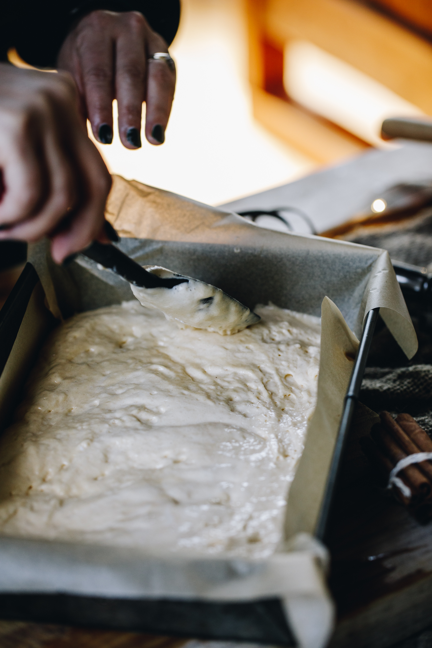 In a baking tin is unbaked sponge mixture for the mini berry trifles. The mixture is being smoothed out on a wooden table. 