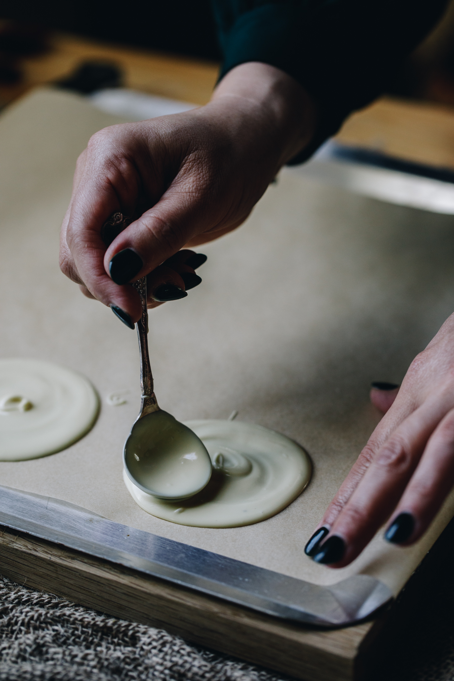 On a silver tray covered with brown paper white chocolate is being smoothed in to discs. 