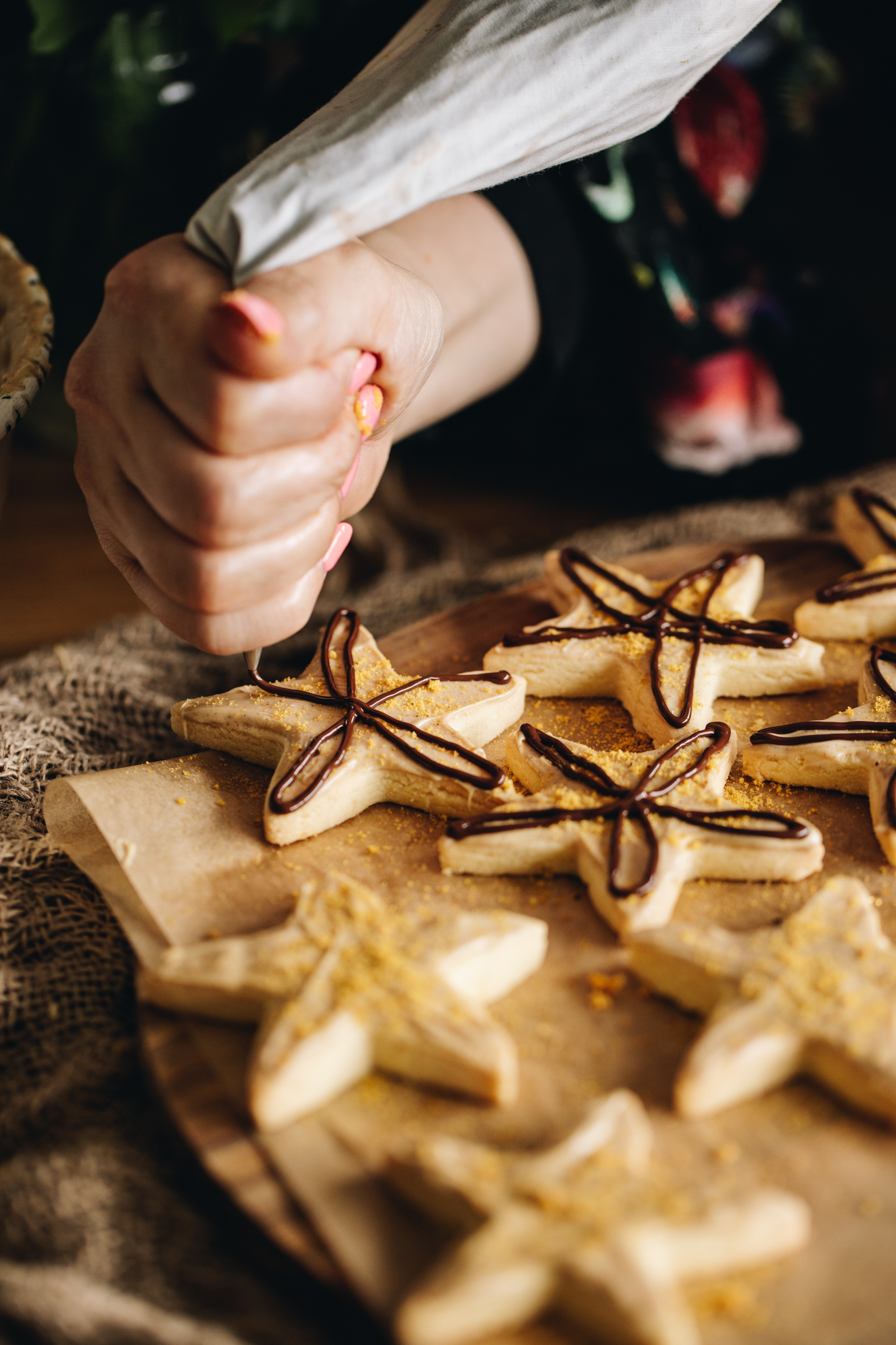 On brown baking paper is freshly baked lemon shortbread cookies. They all have white chocolate on them but Naomi is decorating one by piping dark chocolate on top of it.