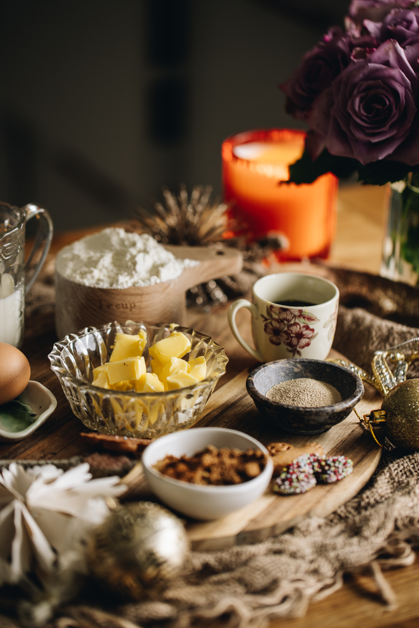 Sticky gingerbread scroll ingredients are in different vintage bowls and are sitting on a wooden board on top of wooden table There is a bunch of purple flowers next to the ingredients.