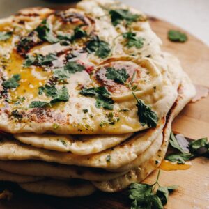A pile of freshly baked garlic butter naan bread is piled on a wooden board.