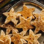 Decorated Lemon shortbread cookies have white chocolate and golden sprinkled on top and are piled on a silver tray.