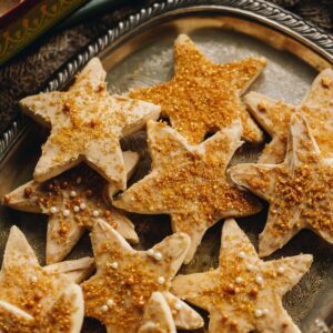 Decorated Lemon shortbread cookies have white chocolate and golden sprinkled on top and are piled on a silver tray.
