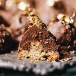 Close up of a chocolate hazelnut cookie that has been sliced open to reveal the hazelnut biscuit, hazelnut cream and the hazelnut inside.