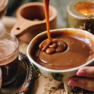 A close up shot of homemade salted caramel sauce is being drizzled in to a small ceramic bowl. It is thick and smooth.