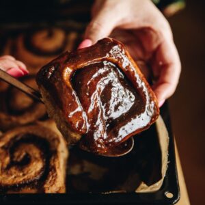 A sticky gingerbread scroll is being lifted out of the tray with a spoon which reveals the sticky glaze that comes off the base of the scrolls.
