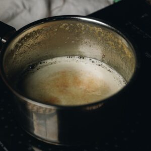 Brown butter is in a pot that is foaming and brown speckles have floated to the top
