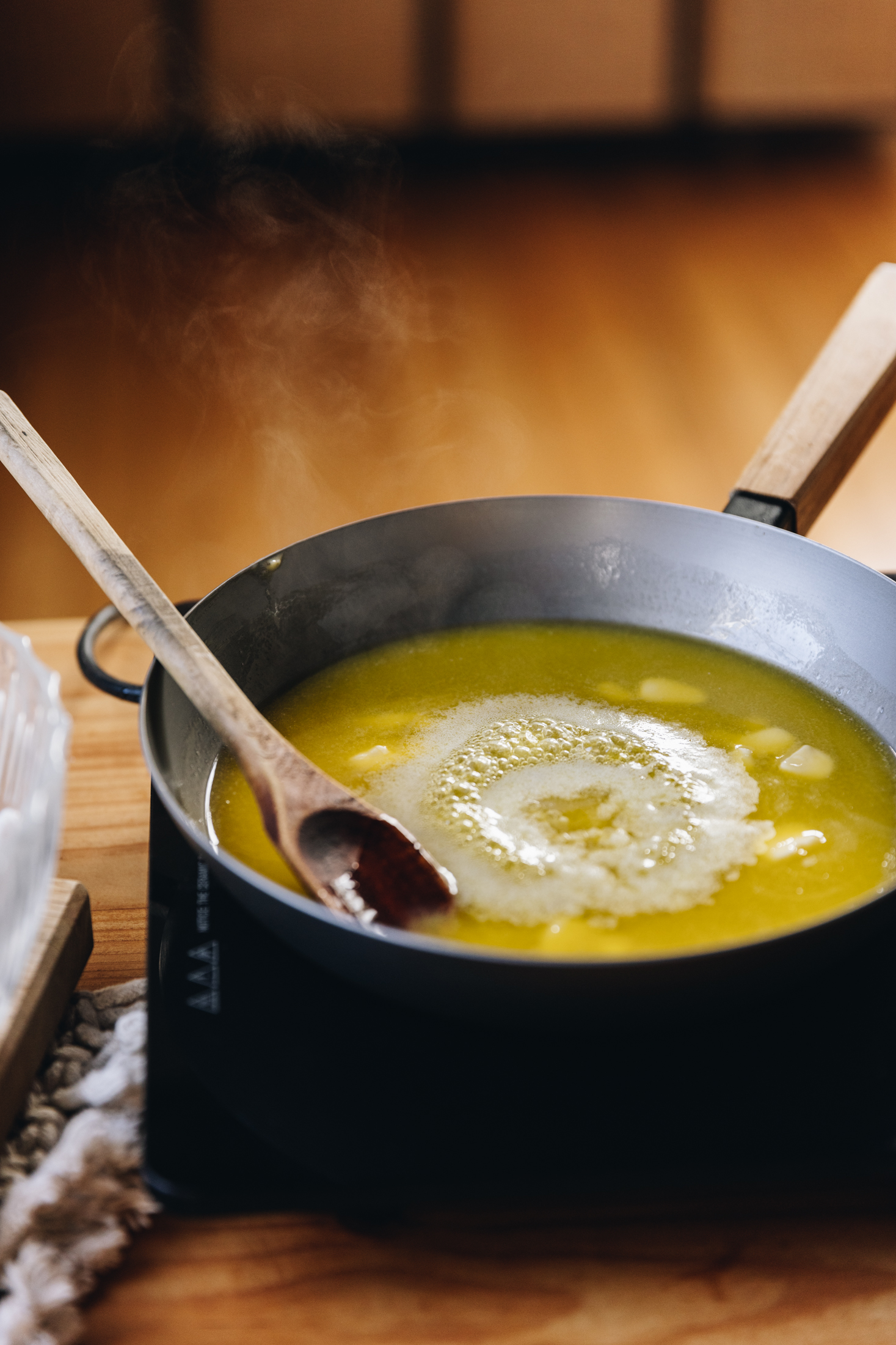 In a frying pan butter is melted and is starting to foam. A wooden spoon sits in the centre of the pan.