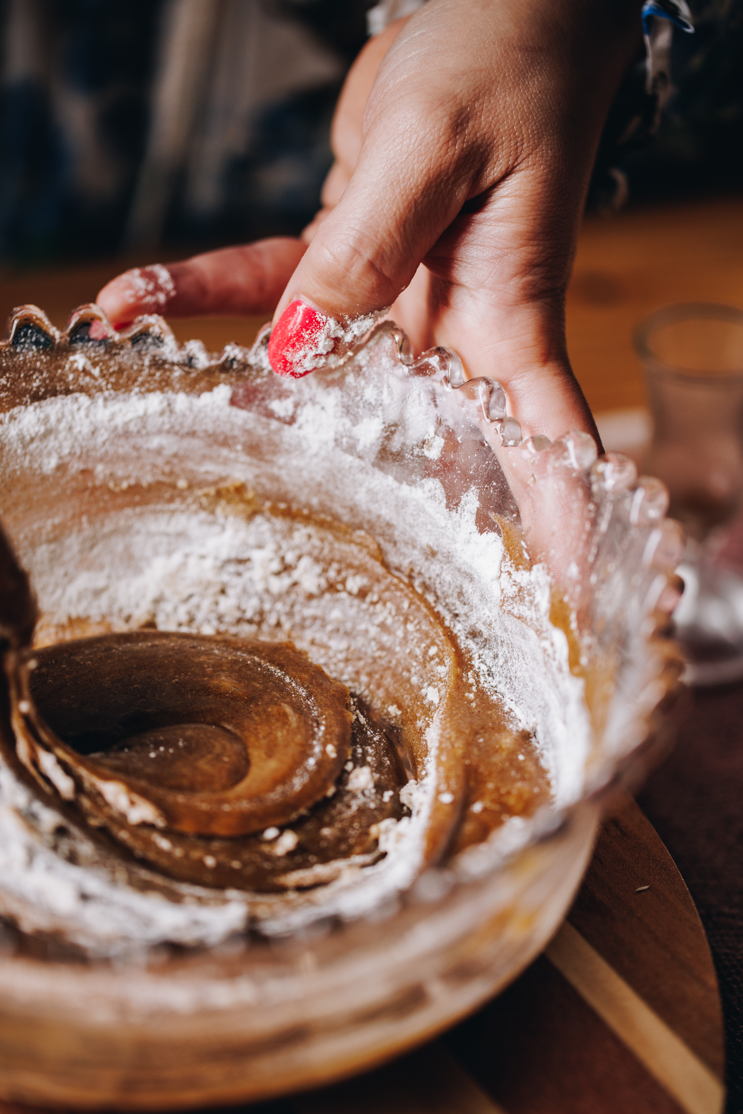 The brandy snap mixture is in a purple vintage bowl. It is being stirred with flour around the edge. It is on a wooden table. 