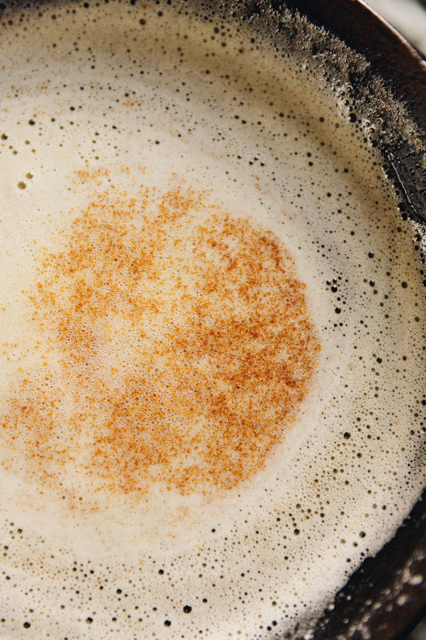 A flatlay shot shows a black frying pan with brown butter foaming in it. In the centre are brown bits that have floated to the top. 